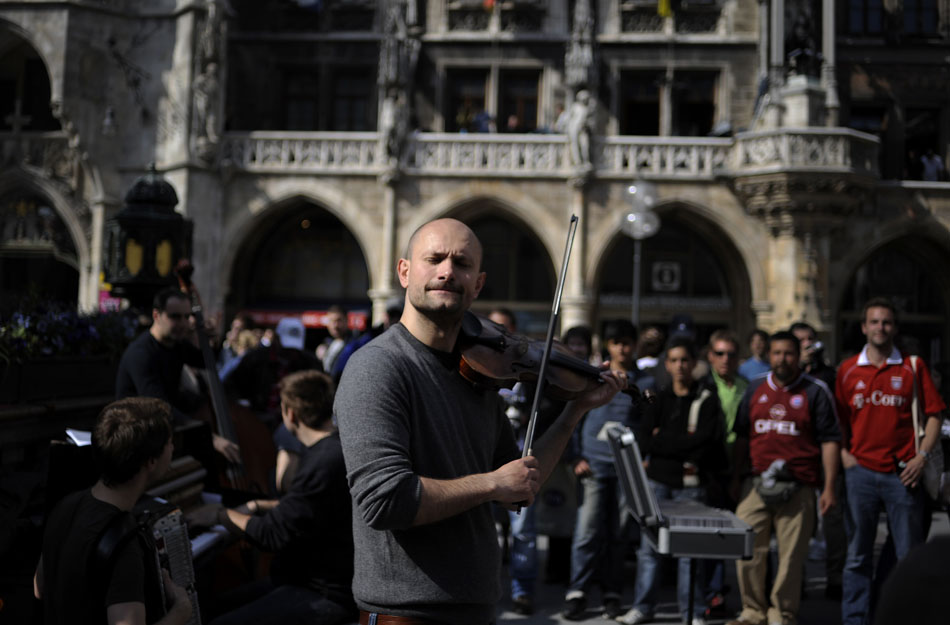A street performer plays a violin for a crowd of tourists on Saturday, May 22, 2010, in Munich's Marienplatz. Good weather attracted several tourists to the city's center to eat and shop.