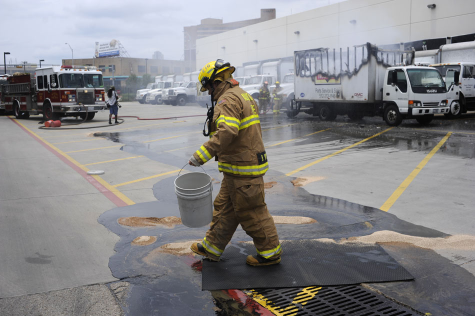 A firefighter spreads a substance to keep oil and fuel from a truck service parts truck out of the sewer as firefighters finish extinguishing the truck in the parking lot of the Austin American-Statesman on Tuesday, June 8, 2010.
