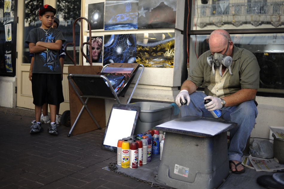 A street artist works on a piece using spray paint as two youngsters, left, back away from the overspray on Saturday, July 31, 2010, in San Antonio, Texas.