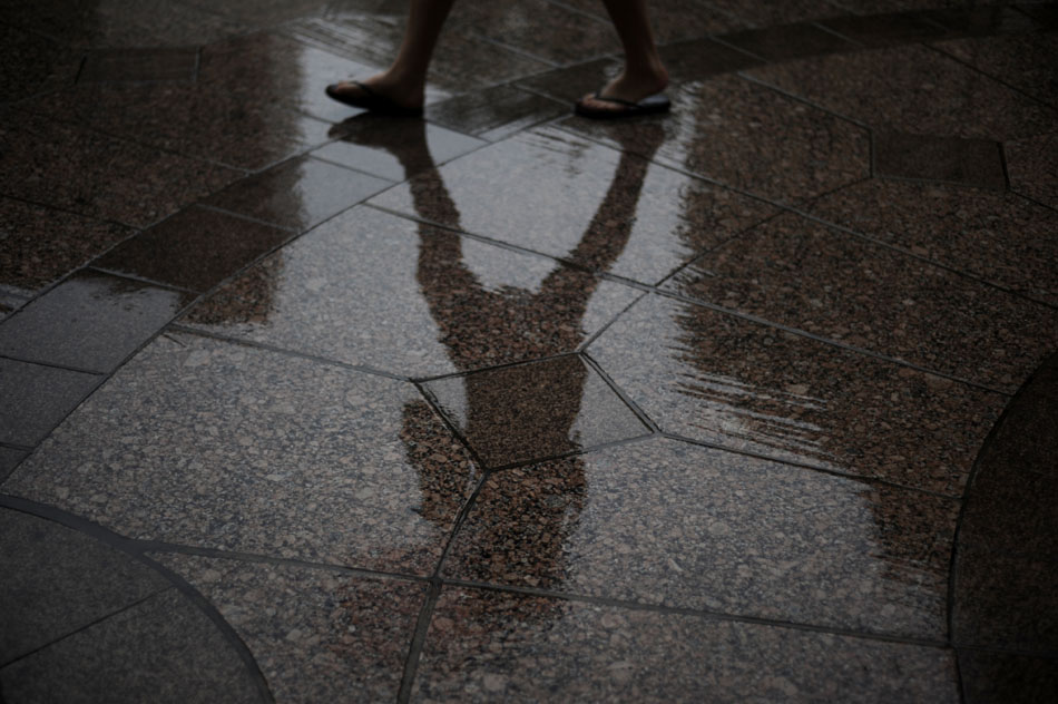 A woman with an umbrella is reflected in a wet sidewalk along Congress Avenue on Friday, July 2, 2010.