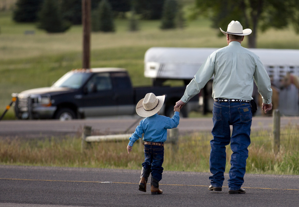 A man crosses the road with his youngster after a chuckwagon breakfast before the Cheyenne Frontier Days cattle drive on Sunday, July 17, 2011, in Cheyenne.