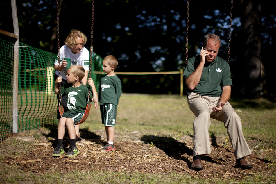Michigan State athletics director Mark Hollis, right, takes a break from a fan event to take a phone call on a swing set as fans Lisa Epple plays with her sons Owen, left, and Wyatt during an event on Tuesday, June 12, 2012, at the Berrien County Sportsman's Club near Berrien Springs, Mich. The stop was part of MSU's Coaches on the Road tour. (James Brosher/South Bend Tribune)