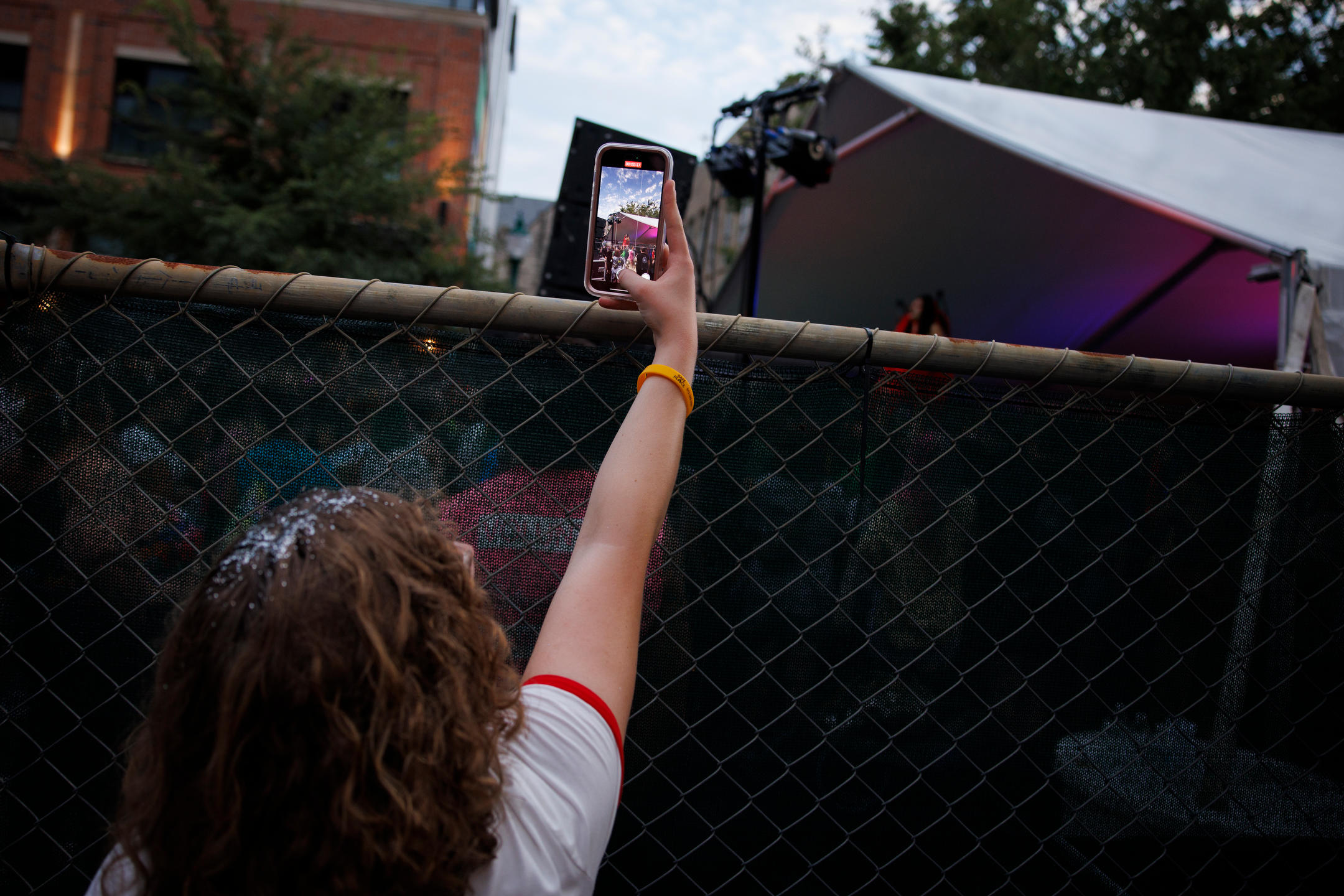 A festival goer reaches over a fence to record a performance by Santana Sword during Bloomington Pridefest on Kirkwood Avenue on Saturday, Aug. 26, 2023. (James Brosher/Indiana University)